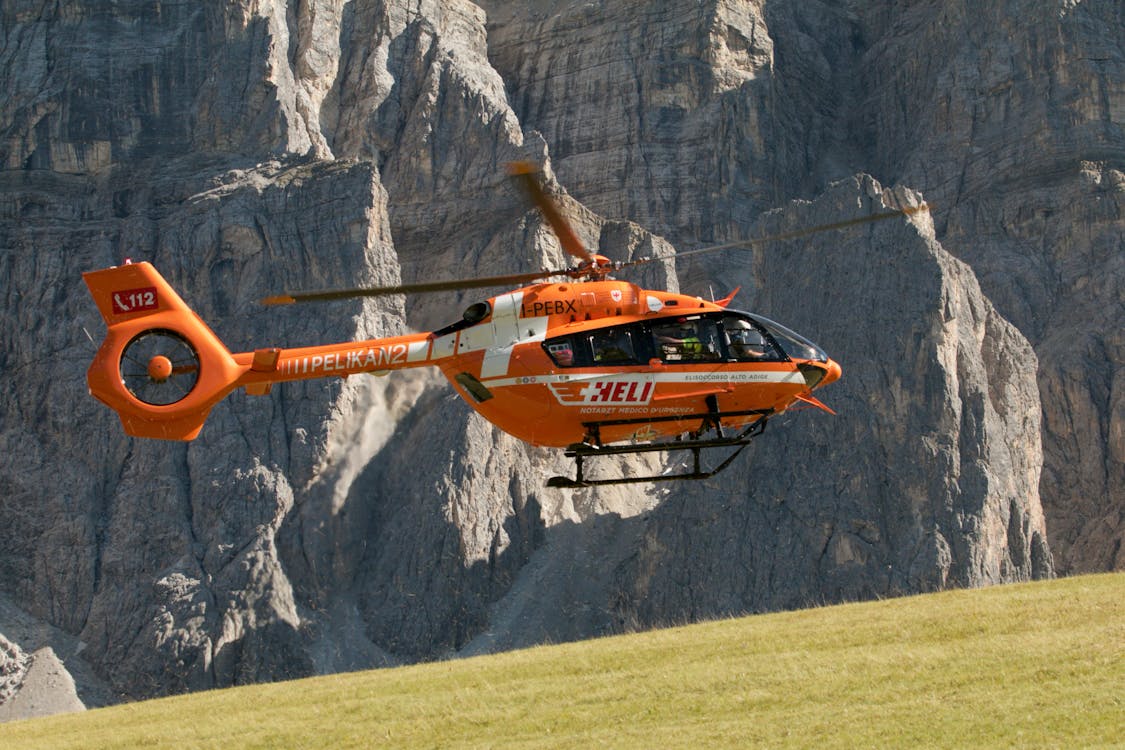 Orange rescue helicopter flying over mountains — alpine rescue costs covered by adventure sports insurance