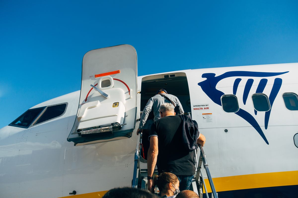 Travelers board a Ryanair plane for their flight under a clear blue sky