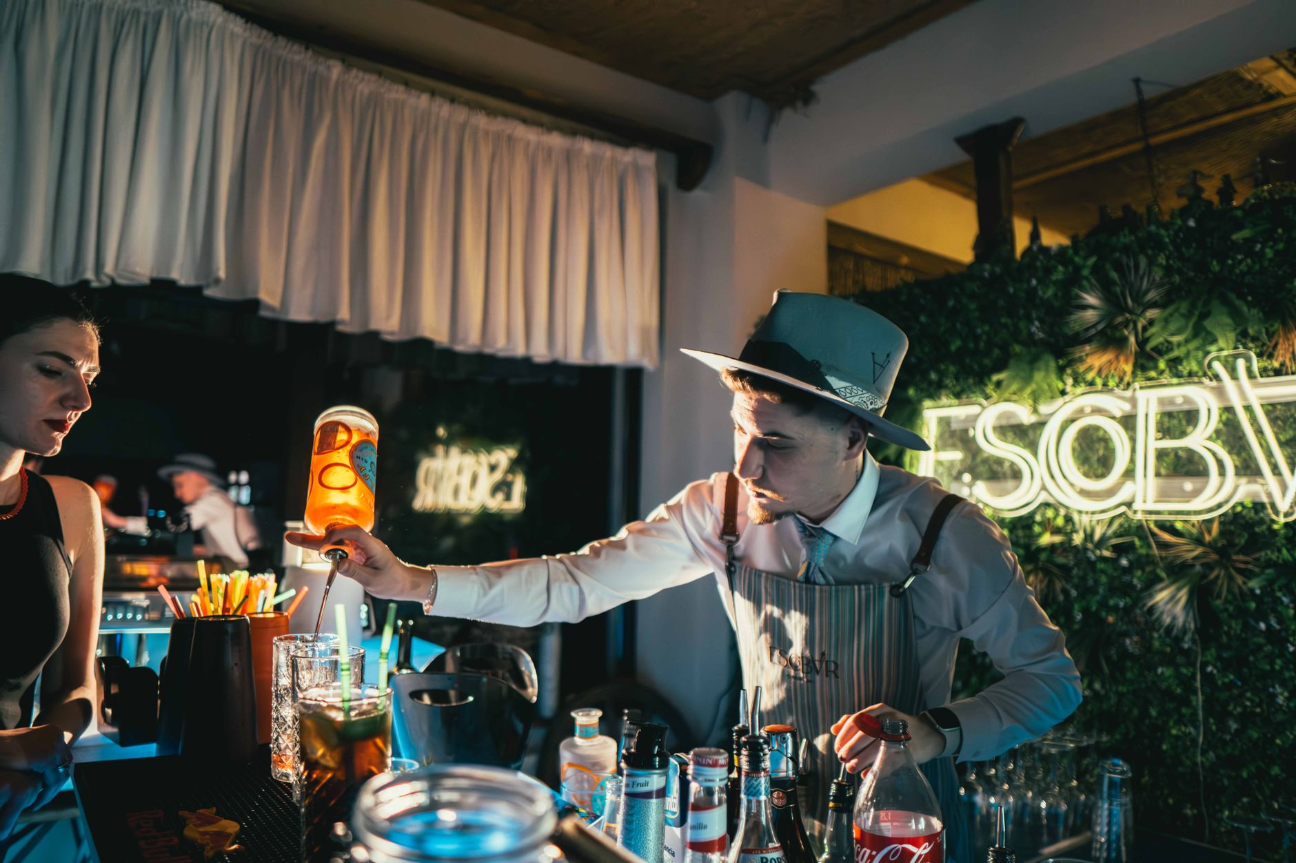 Bartender skillfully mixing a cocktail in a trendy neon-lit bar setting with lively ambian – Which island is better value for a party trip?