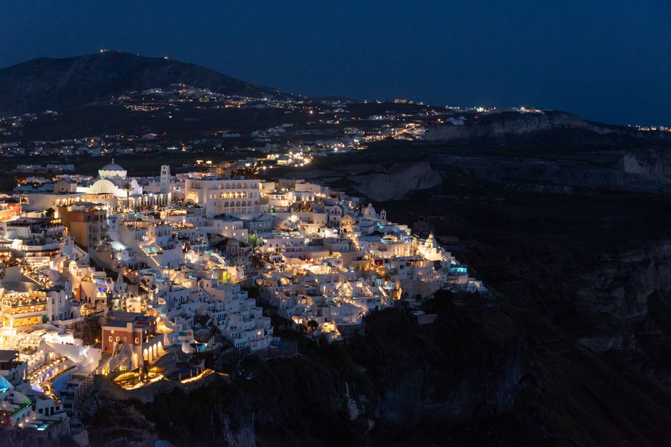Stunning aerial view of Santorini's glowing architecture against a dark night sky. – What is nightlife in Santorini really like?