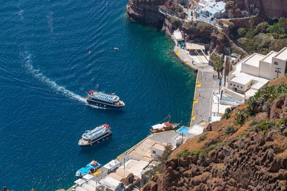 A stunning aerial view of Santorini's old harbor with boats and vibrant blue waters. – Can you party on both islands in one trip?