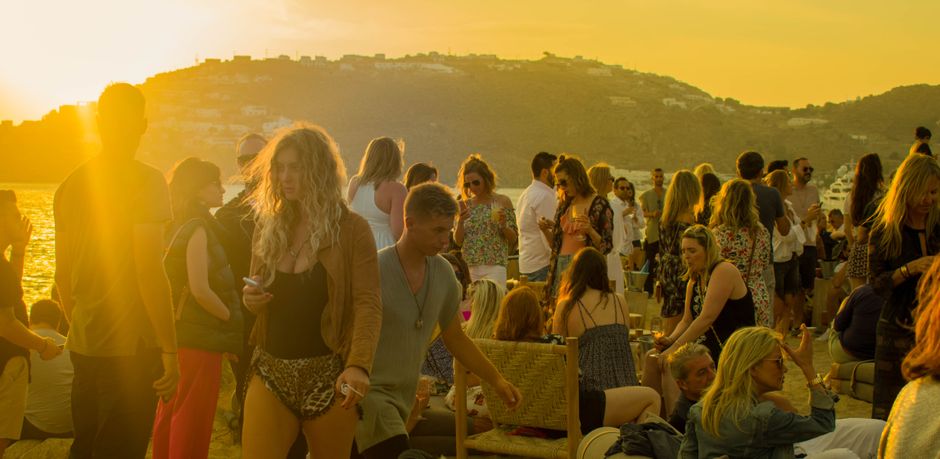 A lively gathering of people enjoying a sunset party on a beach in Mykonos, Greece. – Which should you pick?