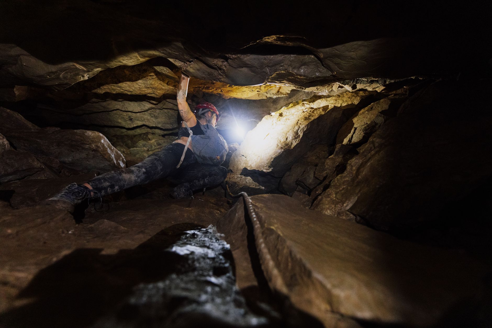 Adventure caving: a caver in helmet and headlamp descending a rope or climbing through an unlit, non-touristy cave passa