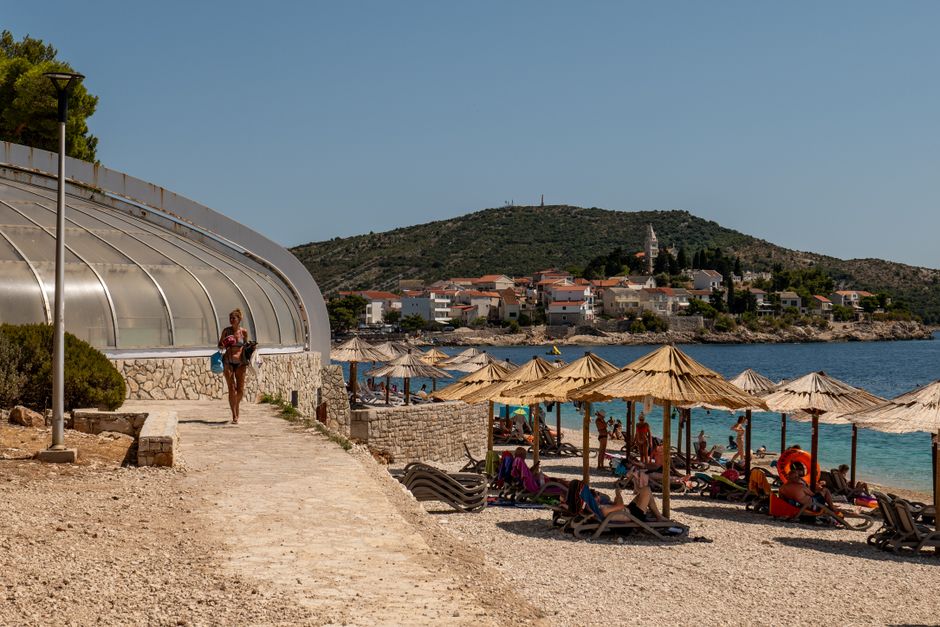 A sunny day at the beach in Primošten, Croatia with tourists relaxing under umbrellas. – Why Croatia Is the Godfather of European Naturism