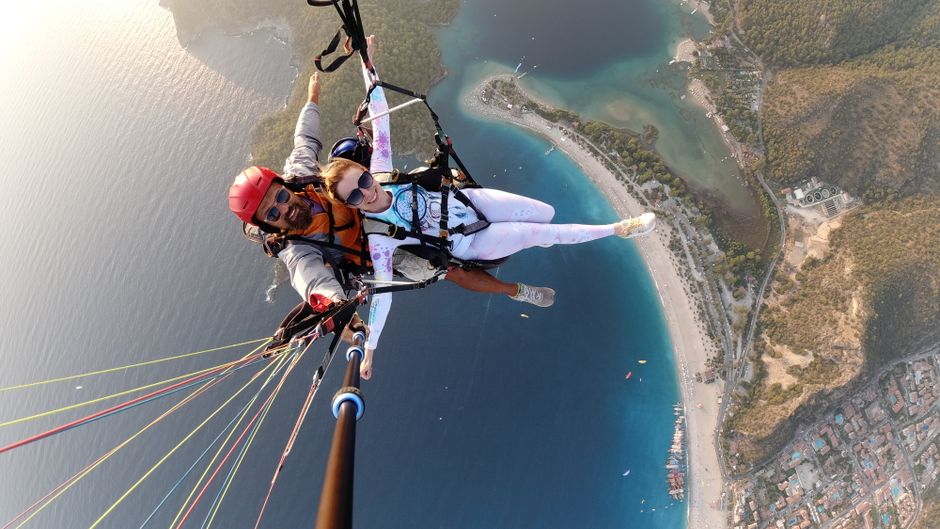 Dynamic aerial view of a joyful couple paragliding above the coastline, capturing an adventurous selfie. – Why Ölüdeniz Is Turkey's Paragliding Capital