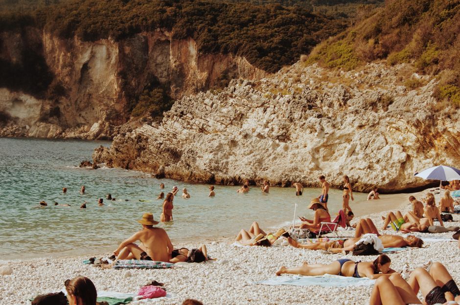 Sunbathers enjoy the beautiful seaside at Liapades Beach in Greece, set against a rocky backdrop. – Is Nudity Actually Legal on Greek Beaches?