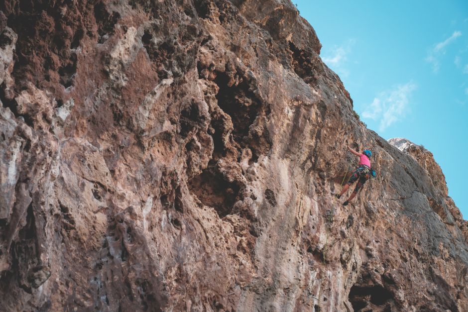 Back view of anonymous female climbing on uneven stony terrain under peaceful bright blue sky – Kalymnos Climbing Festival and Safety Notes (Rebolting Project)