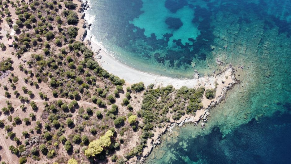 A stunning aerial shot of a Greek coastline with clear blue waters and lush greenery. – Quick Comparison: Which Greek Naturist Beach Fits You?