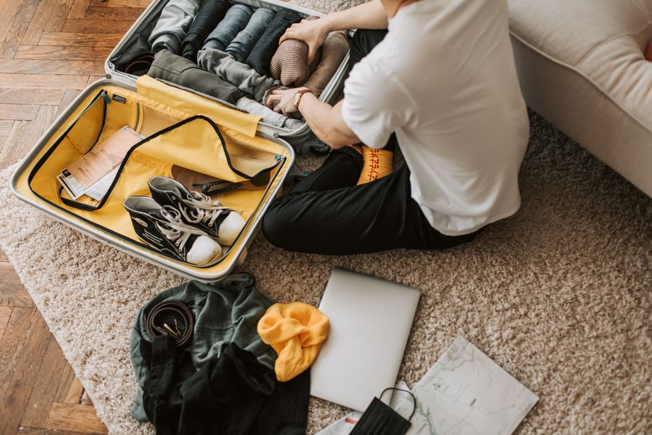Man organizing clothes and essentials into a yellow suitcase for travel in a cozy living room. – How to Get There, When to Go & What to Pack
