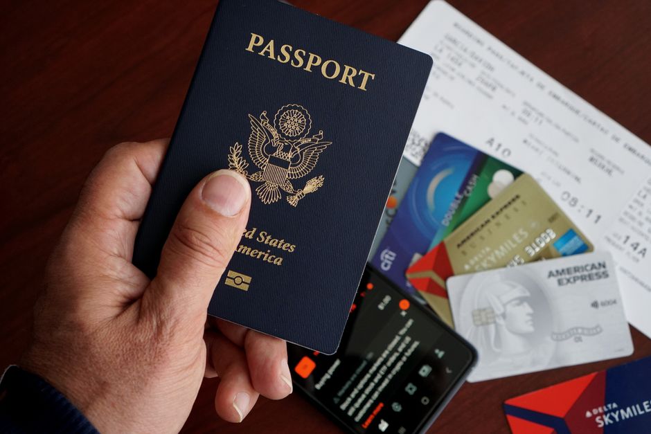 A close-up of a US passport with credit cards, tickets, and a mobile phone on a table. – When Should You Apply for Your First Travel Card?