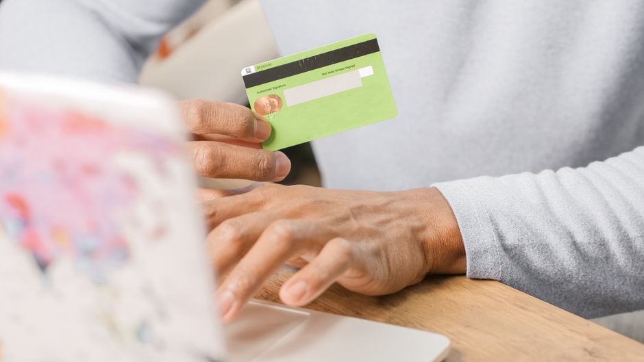 Close-up of hands holding a green credit card for an online purchase using a laptop, depicting secure transactions. – How Big Are Sign-Up Bonuses, and How Do Yo