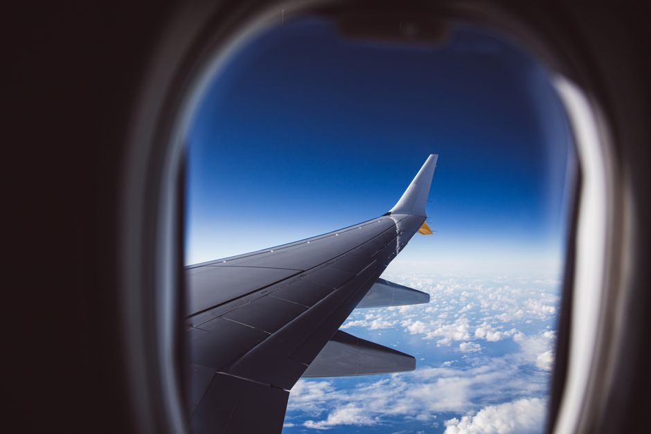 A view from an airplane window showing the wing and clouds below, captured in daylight. – Transfer Partners vs Fixed-Value Redemption: Which Wins?