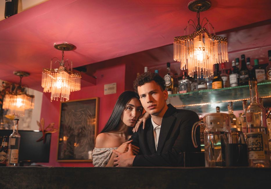 A stylish couple poses at a sophisticated bar, illuminated by warm, ambient lighting and chandeliers. – The Best Lifestyle Clubs for Couples in Amsterdam
