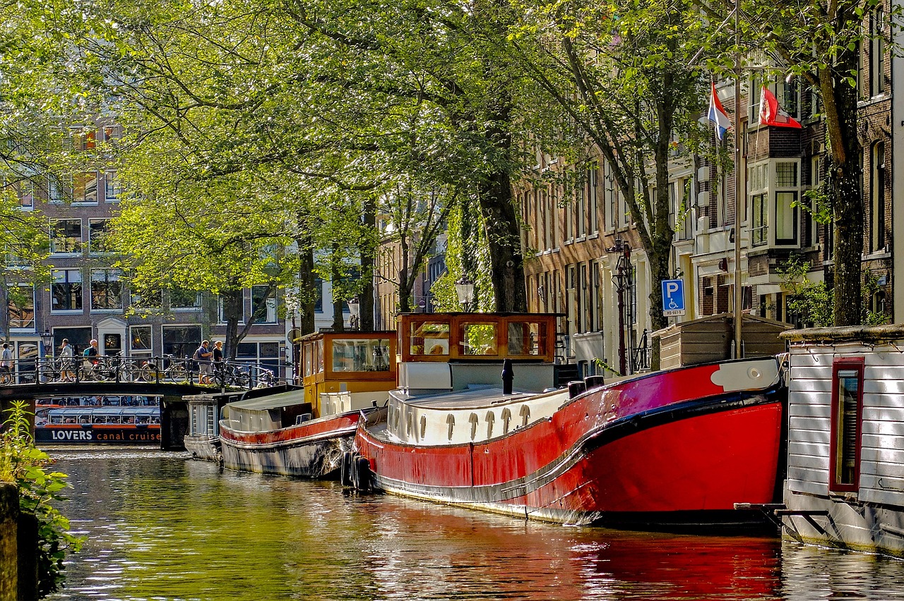 Colorful houseboat moored on an Amsterdam canal beside a Lovers canal cruise boat – Where to Stay and How to Get There