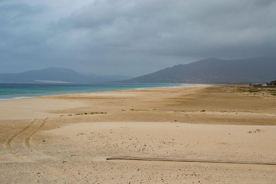 Wide sandy beach under cloudy skies in Tarifa, Spain, offering a serene coastal view. – Where to Kitesurf: Los Lances vs Valdevaqueros Beach