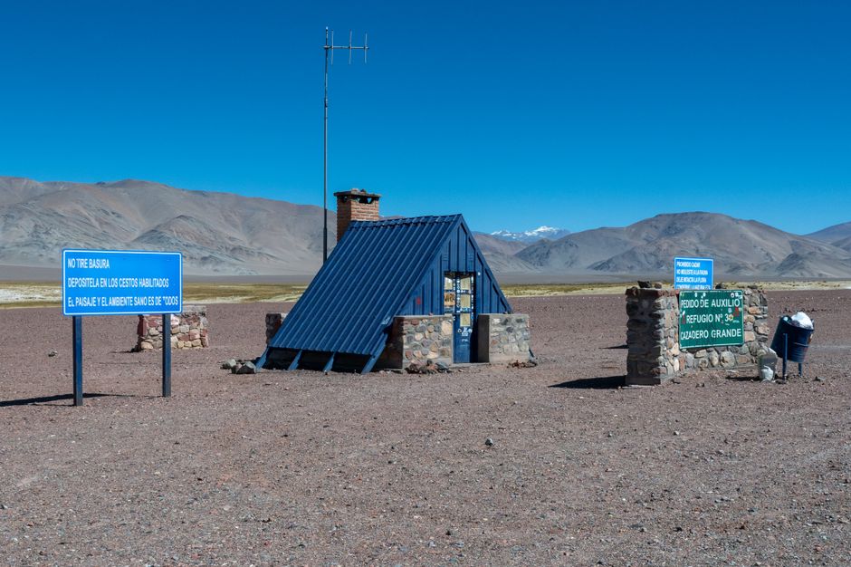 Stone shelter and signs against Andes Mountains in Catamarca, Argentina. – Where to Stay: Refugios and Campsites (Cost Breakdown)