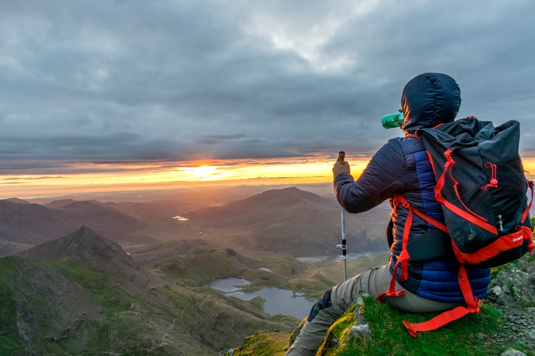 man sitting on cliffhanger looking at mountain under gloomy clouds – Best Time to Hike and How Far in Advance to Book