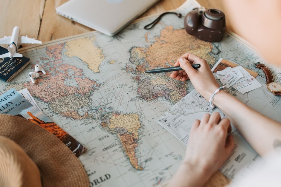 Hands marking destinations on a world map surrounded by travel essentials like passport and camera. β 4. Search "Anywhere" When Your Destination Is Flexible