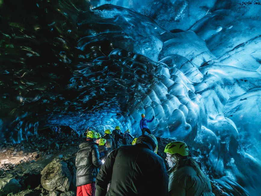 Group of explorers in an illuminated ice cave with vibrant blue hues, wearing helmets and winter gear. – Ice Cave and Glacier Combo Tours