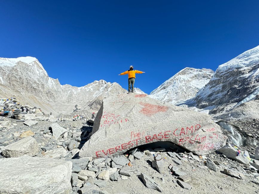 A mountaineer stands on a rock at Everest Base Camp, surrounded by snowy peaks. – How Much Does the Everest Base Camp Trek Cost in 2026?