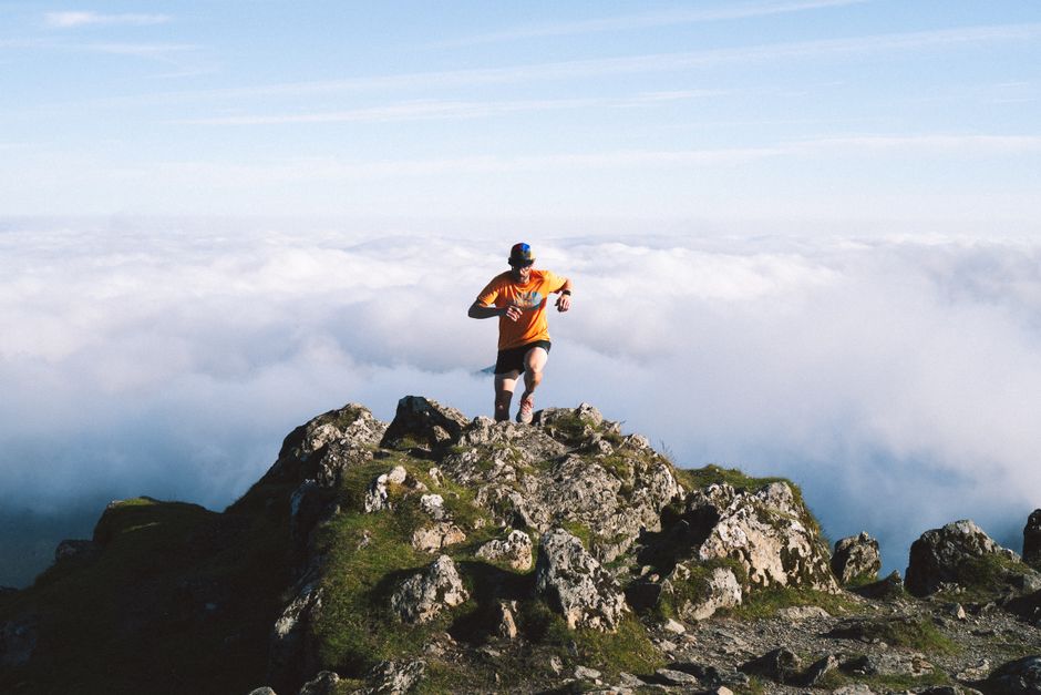 Man running on rocky mountain peak above the clouds, symbolizing achievement and adventure. – Fitness, Training & Altitude Sickness Prep