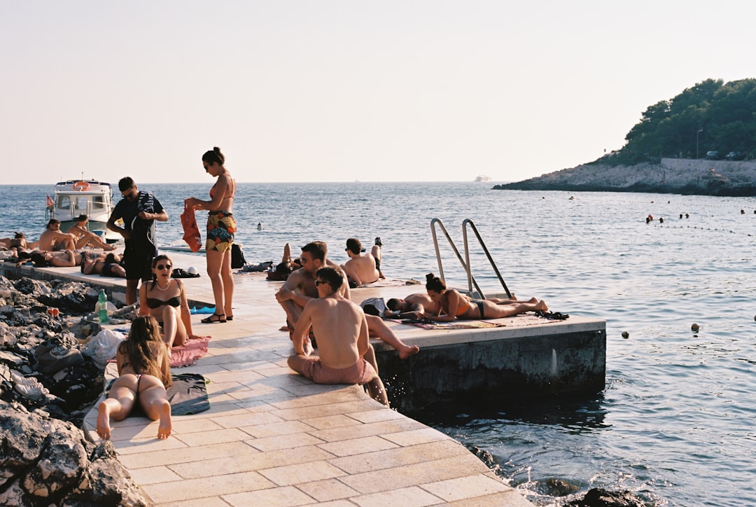 a group of people sitting on a pier next to a body of water – Is Nude Sunbathing Legal in Croatia?