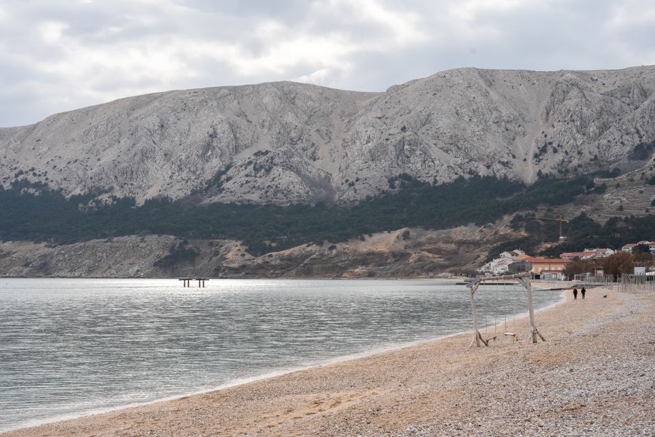 Explore the tranquil beauty of Baska Beach in Krk, Croatia, with mountains and coastal scenery. – Krk and Cres: Quieter FKK Coves Worth the Detour