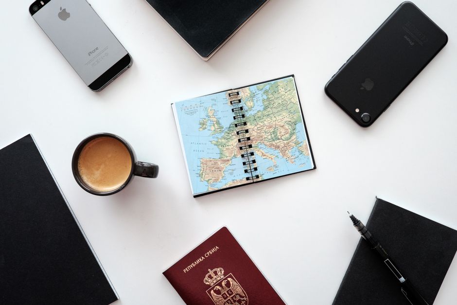 Flat lay of travel essentials with map, passport, and devices on a white surface. – Quick Planning Notes Before You Book