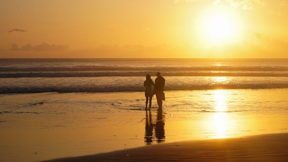 A couple stands on the beach enjoying a warm and romantic sunset together. – Seminyak & Petitenget: Boutique Romance Near the Buzz