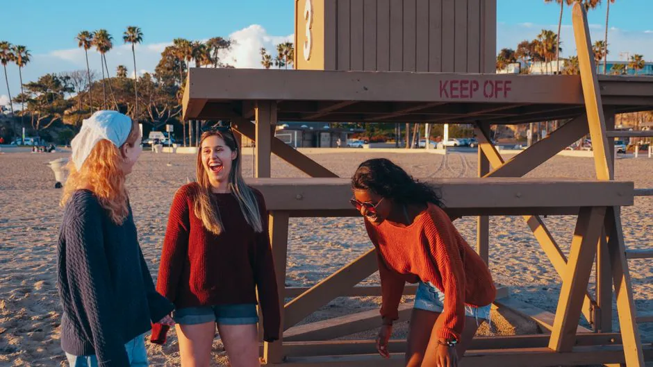 Three friends enjoying a sunset hangout at the beach near a lifeguard tower. – What Is Beach, Please! — and Why Is Everyone Suddenly Talking About It?