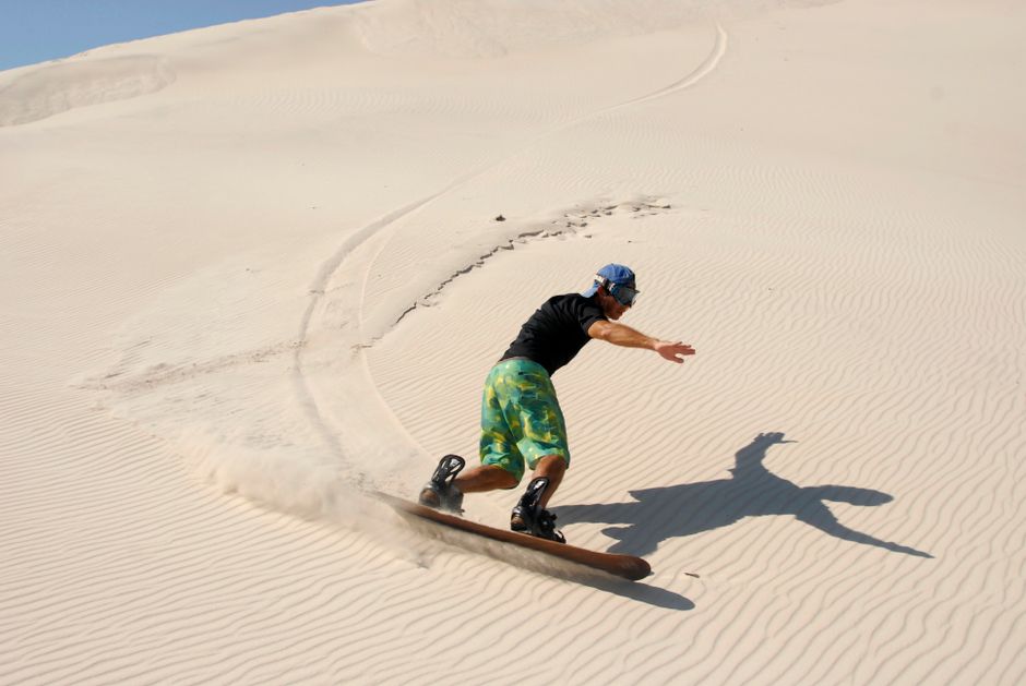 Dynamic sandboarding action in the sunny dunes of Cabo Frio, Brazil. – What Does a Sandboarding Tour Actually Involve?