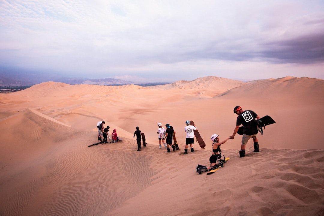 a group of people standing on top of a sand dune – Is Sandboarding in Huacachina Safe?