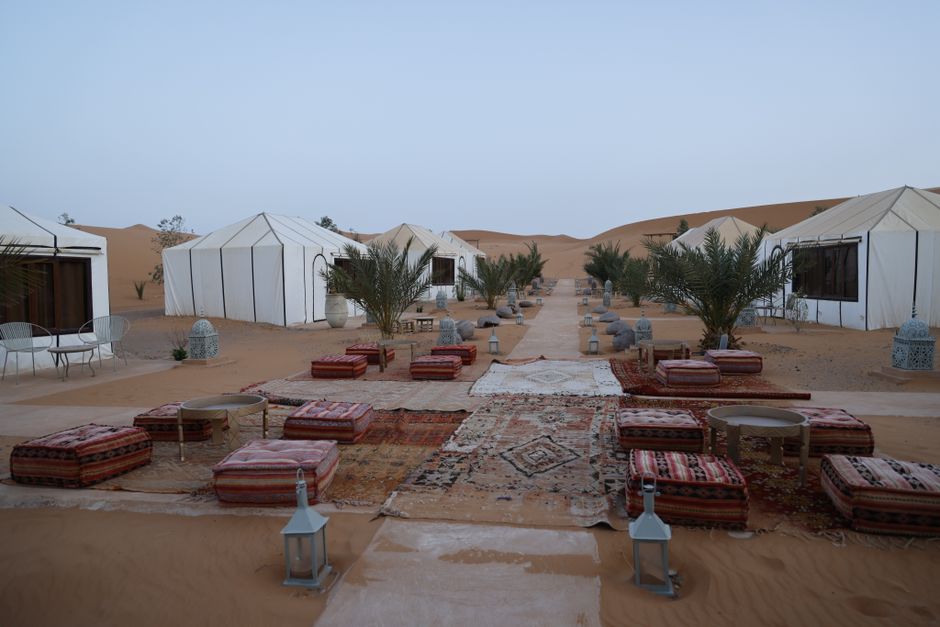 A serene outdoor setup in a desert camp featuring traditional tents, cushions, and lanterns. – Where to Stay Around the Oasis