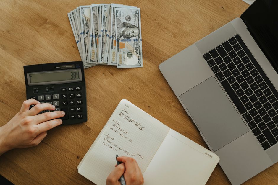 Hands using calculator and notebook, planning finances, with cash and laptop on wooden table. – How Much Does Annual Multi-Trip Insurance Cost in 2026?