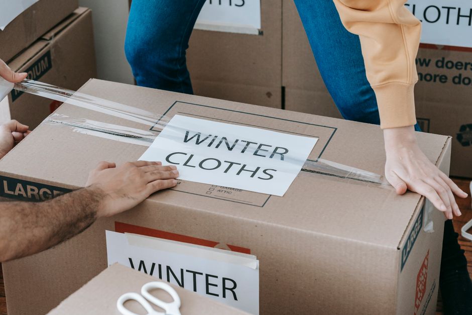 Close-up of hands packing a box labeled 'Winter Clothes' for relocation, emphasizing organized moving. – What Should You Pack Into Your Pre-Move Checklist?