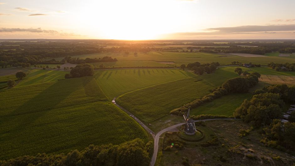 A mesmerizing aerial photo capturing the lush green fields and a windmill in the Dutch countryside at sunset. – What Happened to Defqon.1 2026?