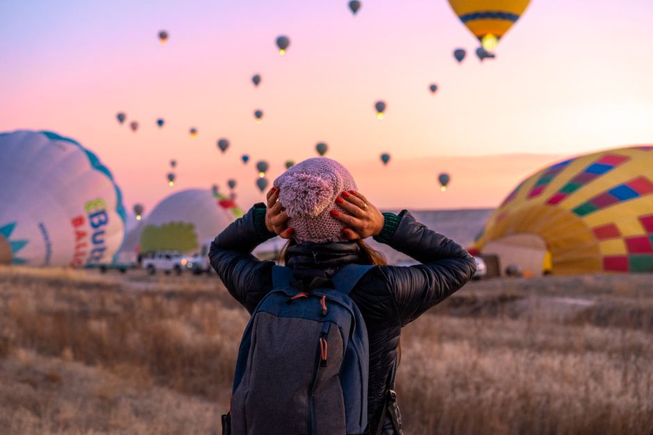 Woman enjoying a view of hot air balloons taking off in Cappadocia, Turkey at sunrise. – What to Wear and Bring on a Sunrise Balloon Flight