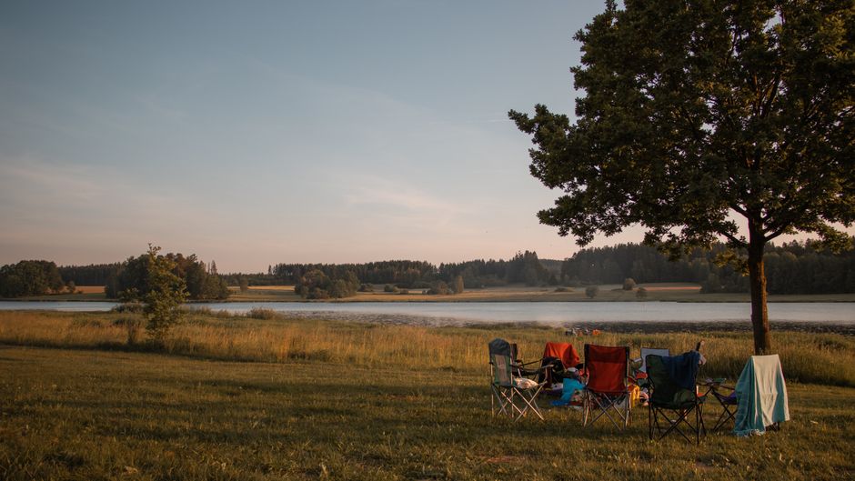 Peaceful lakeside campsite in Treffelstein, Germany with folding chairs under a tree. – What a Weekend on the Holy Grounds Actually Looks Like