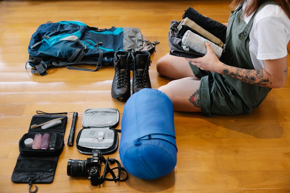 Woman organizing camping gear and clothes on wooden floor indoors, preparing for an adventure. – Packing and Survival Checklist