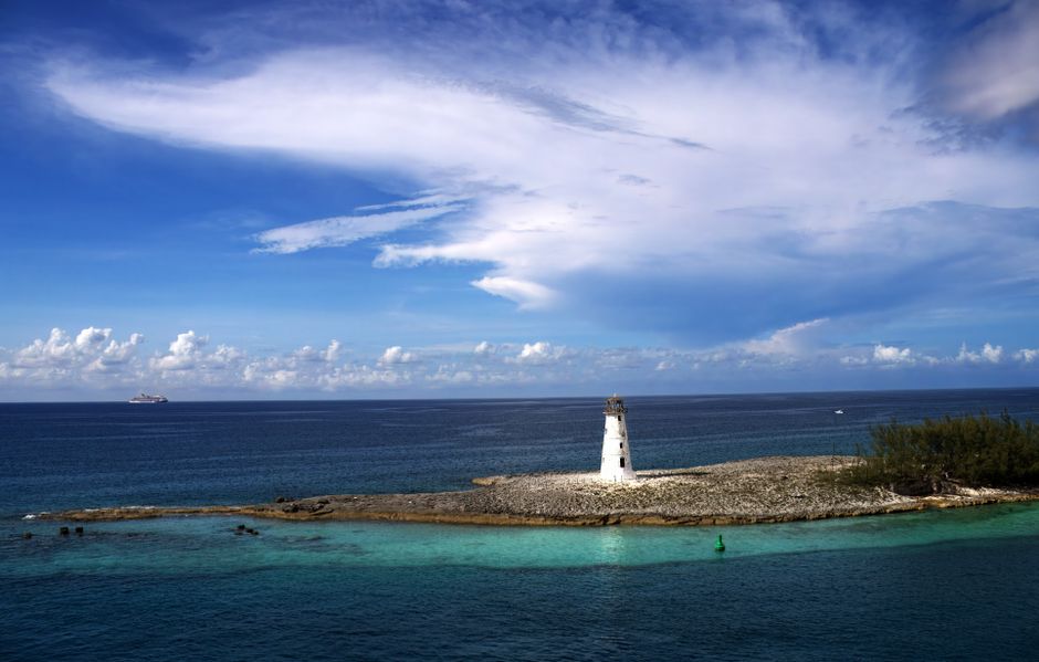 Explore a serene view of a solitary lighthouse on Nassau's rocky coastline under a vibrant sky. – How to Get to the Swimming Pigs From Nassau or Exuma