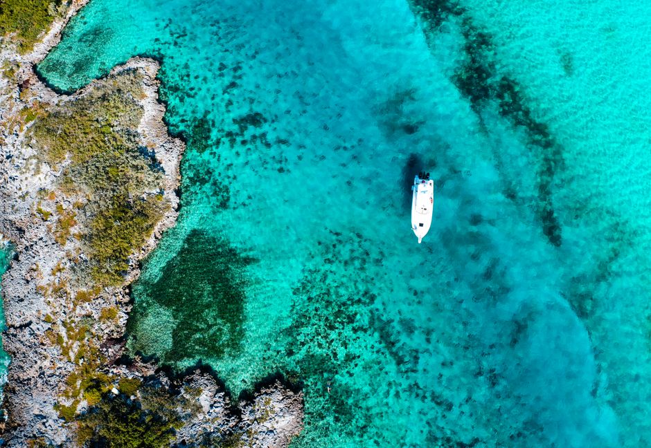 Aerial shot of a boat floating in the turquoise waters of the Bahamas, showcasing vibrant coral reefs. – How Much Does a Bahamas Pig Beach Tour Cost?