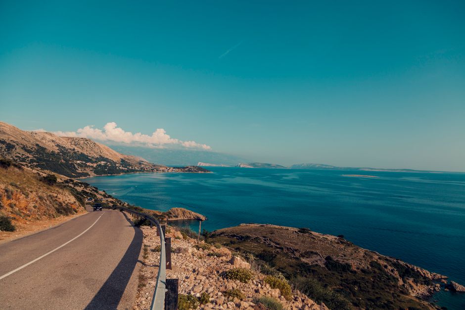 Breathtaking view of a coastal road alongside the ocean with clear blue skies and rugged terrain. – Getting to Croatia's Naturist Coast