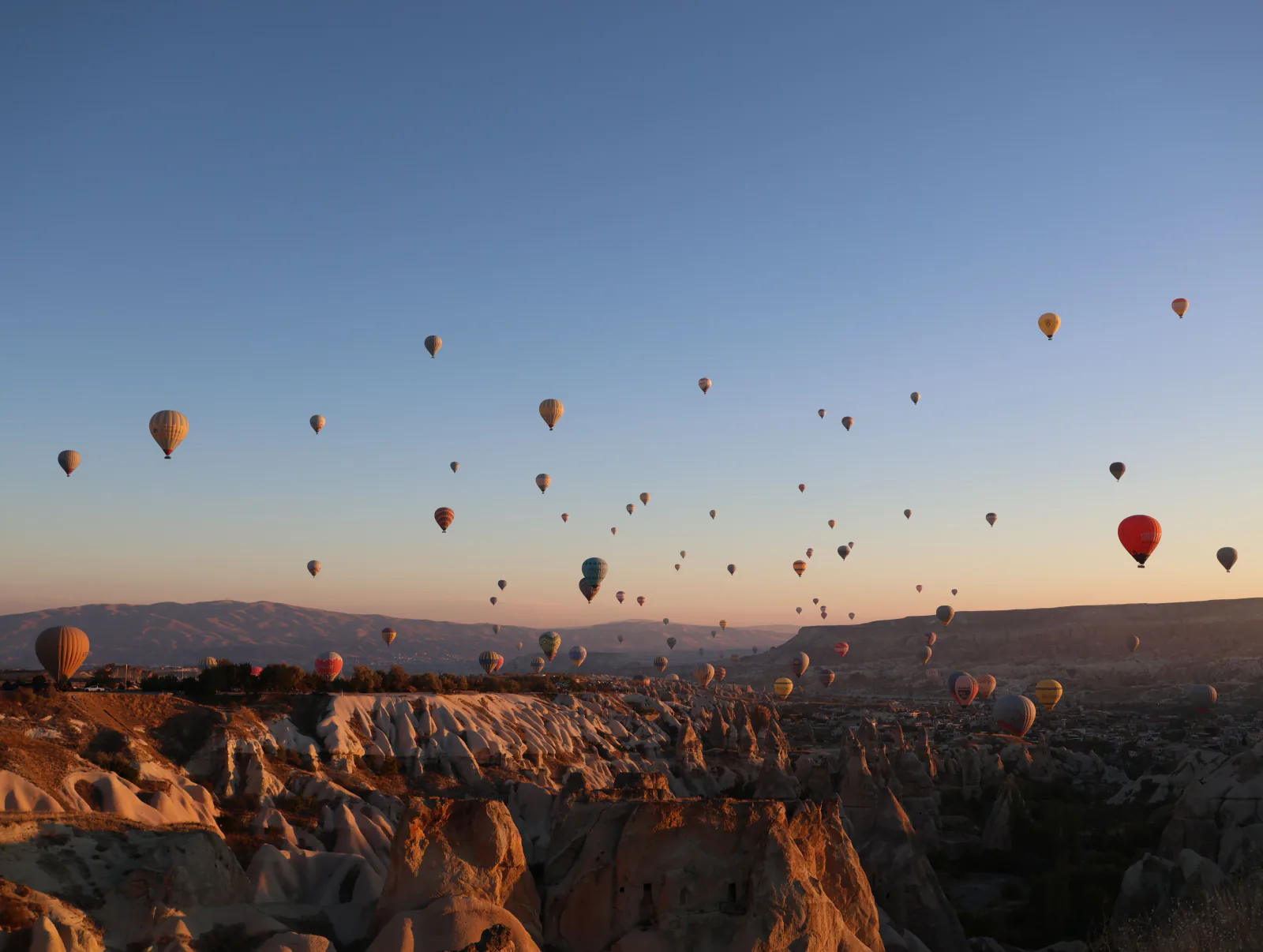 A stunning view of numerous hot air balloons floating over Cappadocia's unique rock formations at sunrise. – How Much Does a Hot Air Balloon Cost in Cappadocia?