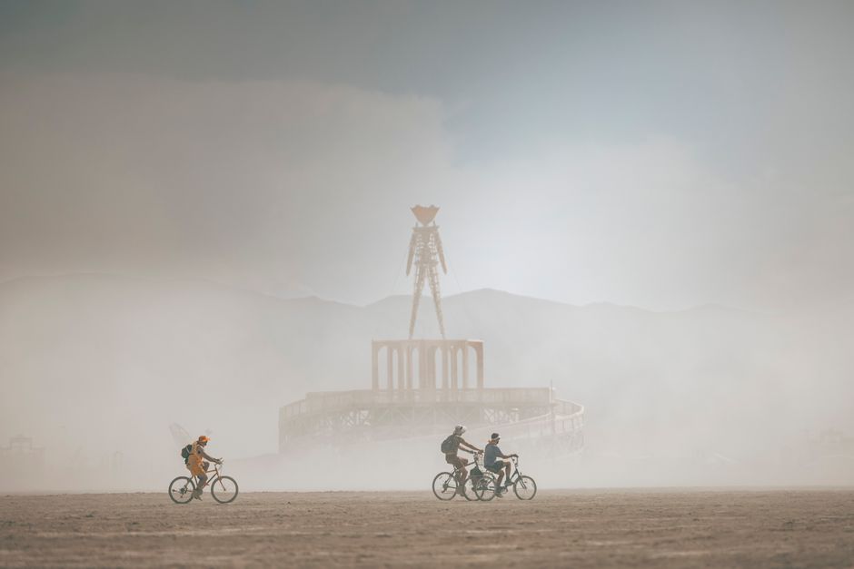 Three cyclists ride through dust at Burning Man festival near the iconic effigy. – What to Pack for the Playa: Dust, Heat and Sudden Storms