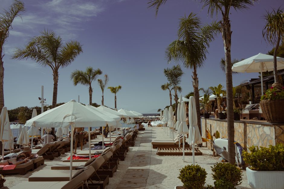 Relaxing beach with palm trees and deck chairs in Ksamil, Albania, under a clear sky. – The Best Beach Clubs in Ksamil