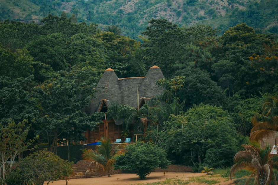 A rustic lodge with a thatched roof surrounded by lush greenery and hills. – Where to Stay Near Bwindi Impenetrable Forest