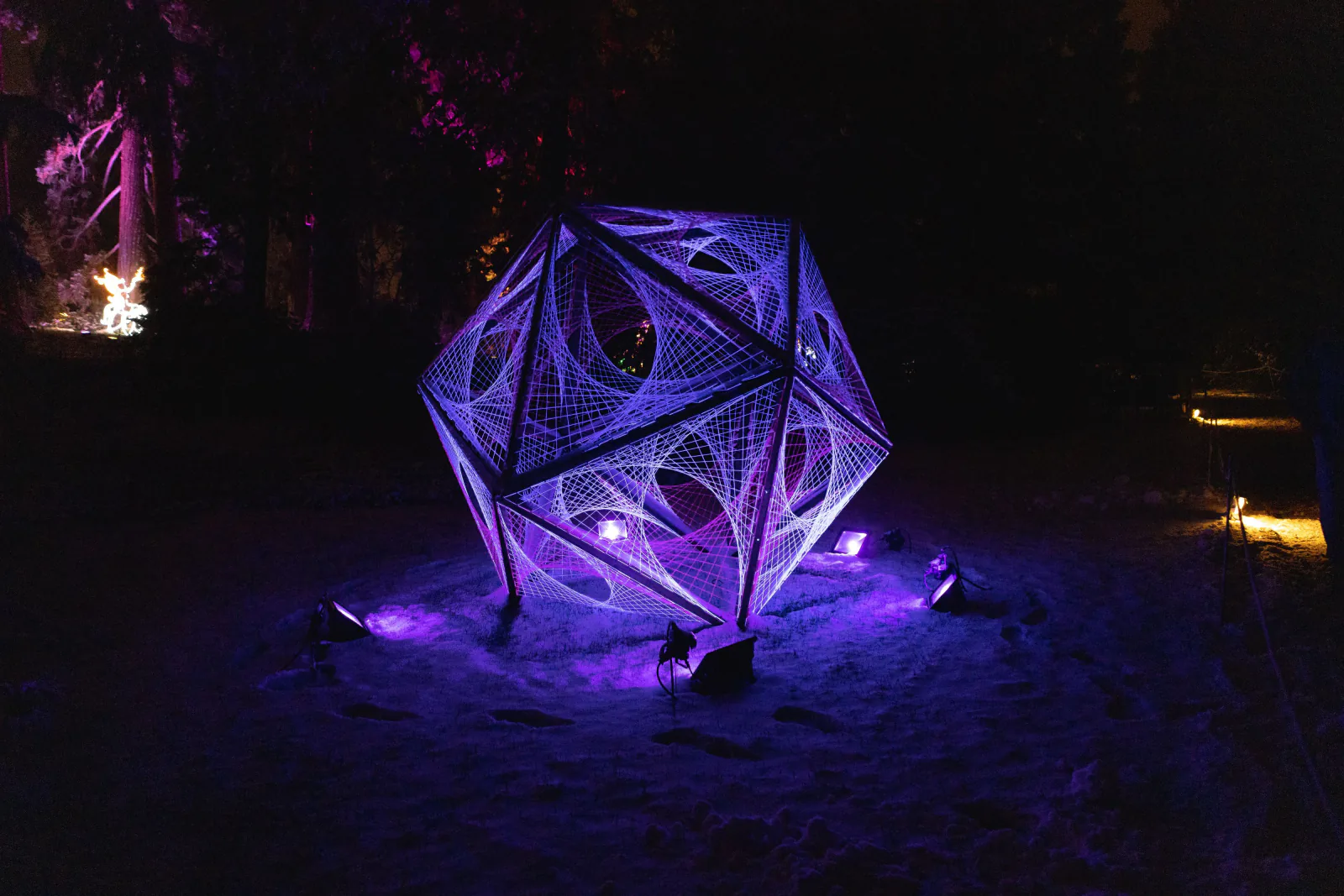 Illuminated geometric art sculpture glowing at night among trees at Boom Festival Portugal