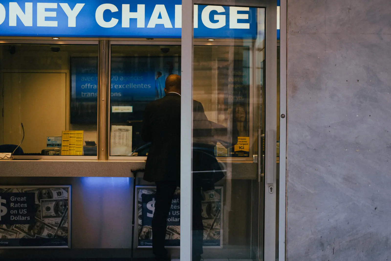 Traveler at a currency exchange office window with posted rates, illustrating why to skip airport exchange counters