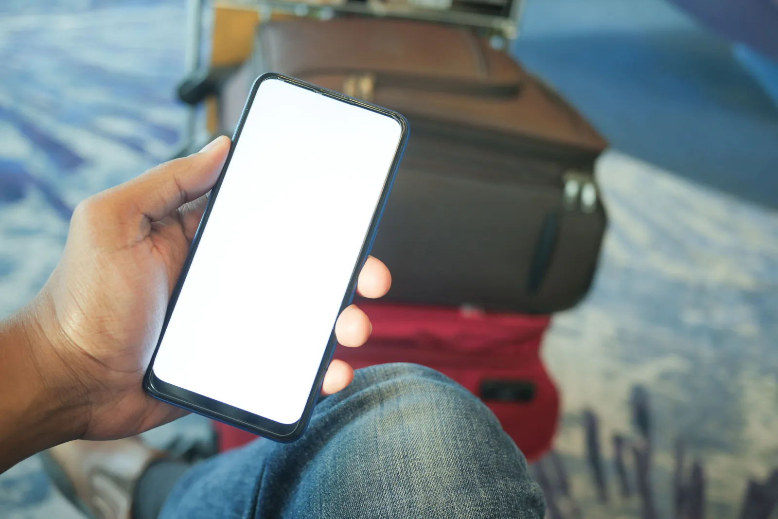 Hand holding a smartphone beside packed luggage, checking a banking app before a flight