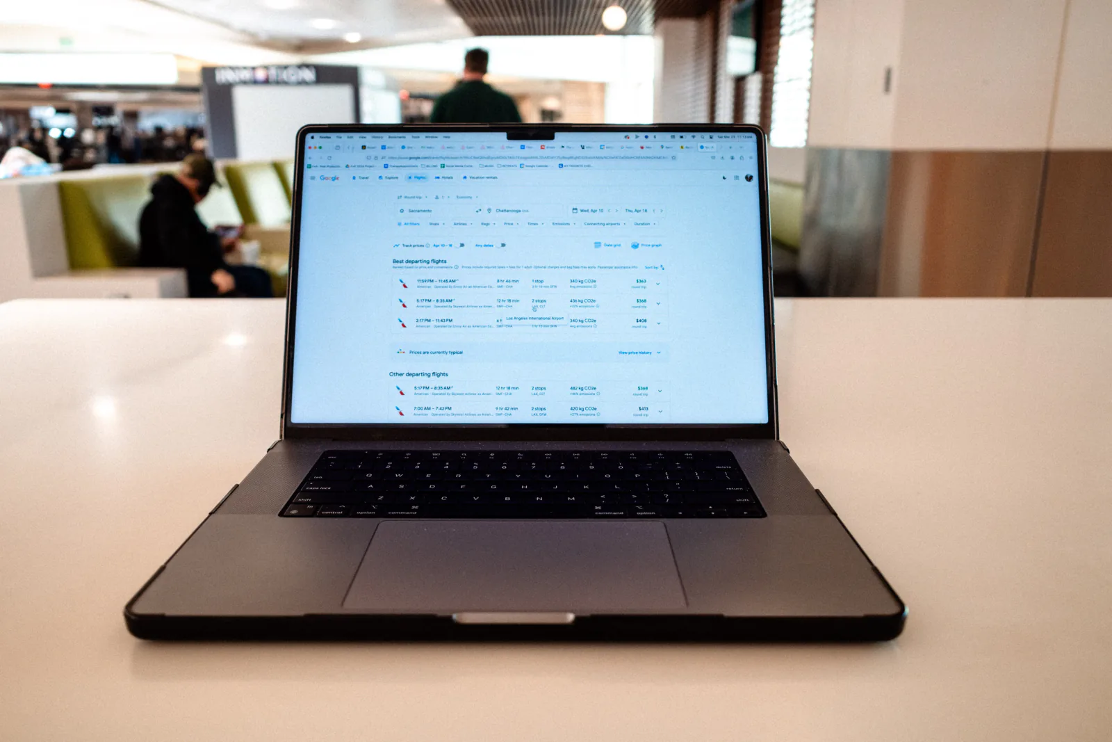 Laptop displaying a flight search results page on a table in an airport terminal